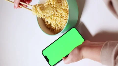 Female using smartphone while eating pasta at home. Smartphone with green Stock Footage 304900254