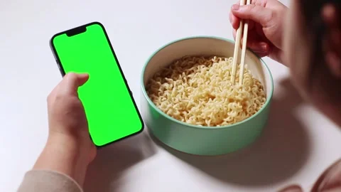 Female using smartphone while eating pasta at home. Smartphone green screen Stock Footage 307752118
