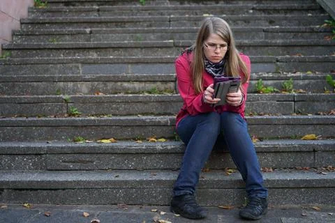 Female using tablet sitting on steps outdoors 库存照片