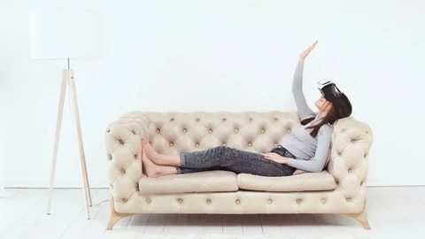 Female using Virtual Reaity helmet on sofa. VR glasses on white caucasian girl. Stock Footage 86429724