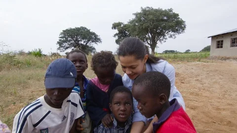 Female volunteer with African charity organisation shows children her smartphone Stock Footage