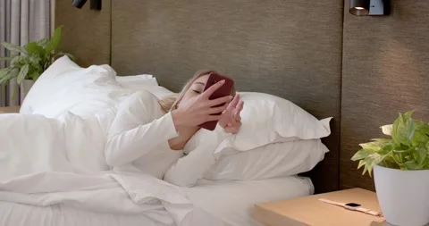 Female waking, reaching for red phone on nightstand picking up and checking it Stock Footage 346613635