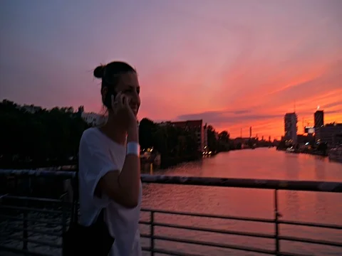 Female walking on the bridge at sunset, having conversation using her smartphone Stock Footage 80541350