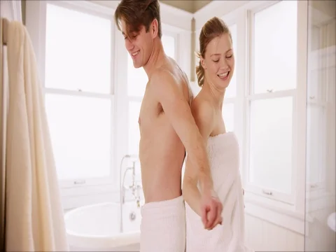 Female walking off camera and removing towel, throwing it to shocked boyfriend Stockbeeldmateriaal 77240127