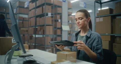 Female warehouse associate scans parcel using tablet computer, works with online Stock Footage 307616509