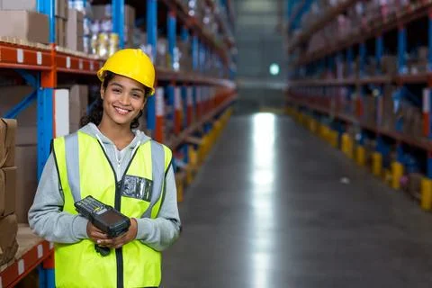 Female warehouse worker using barcode scanner in warehouse aisle with hard hat Stock Photos