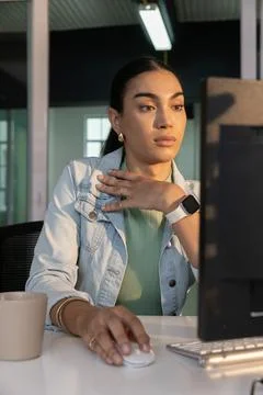 Female worker in denim jacket using wireless mouse touching chest working at Stock Photos