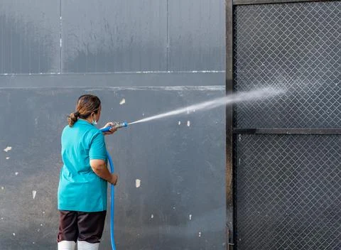 Female worker spraying high-pressure water hose onto metal mesh gate during.. 스톡 사진