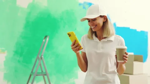 Female worker standing, texting with clients during painting the wall and Stock Footage 247455435