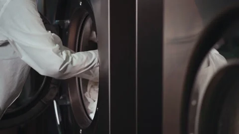 Female worker in uniform loading bed linen in washing machine at laundry Video stock 145804899
