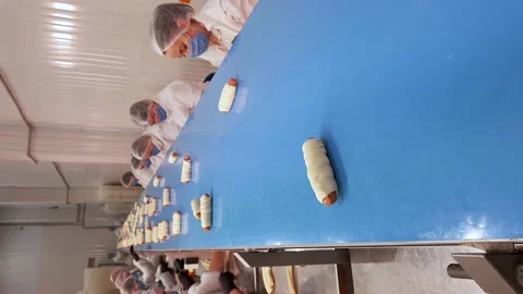Female workers making buns of dought and sausages, put it on conveyor belt. Stock Footage 166470297