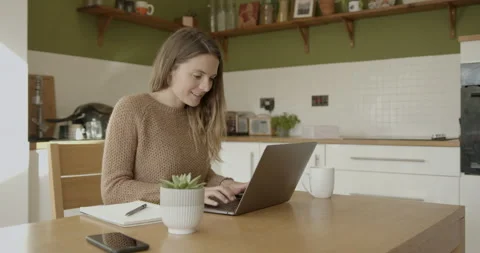 Female working from home at kitchen table using computer laptop and drinking Stock Footage 141846963