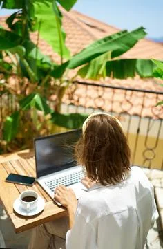 Female working remotely on the laptop computer while sitting on balcony hotel Stock Photos
