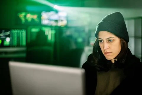 Female young hacker working on computer in dark room programming code 写真素材