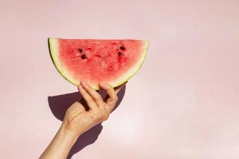 Feminine hand holding slice of ripe watermelon over pink backgroun Stock Photos