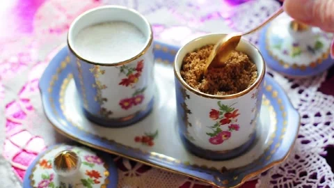 Feminine hand using a tiny golden spoon to stir brown and white sugar in a Stock Footage 339281366