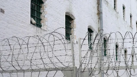 Fence with barbed wire and white prison building, close-up Stock Footage 77876504