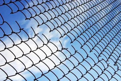 The fence of broken wire netting on the background of blue sky Stock Photos