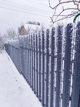 A fence covered in snow next to a tree Stock-Fotos