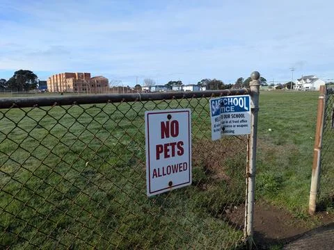 Fence-mounted “No Pets Allowed” notice contrasts open green field Stock Photos