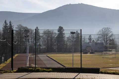 A fenced athletic track and grass field sit beneath tall mountains during a Stock Photos