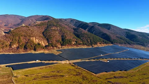 Fenced solar array on green pasture with cattle below mountain ridge. Clear Stock-Footage 336783329