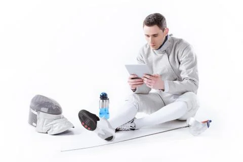Fencer in uniform using digital tablet while resting after training on white Stock Photos