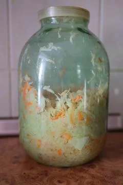 Fermented cabbage and carrots inside a large glass jar in a kitchen Stock Photos