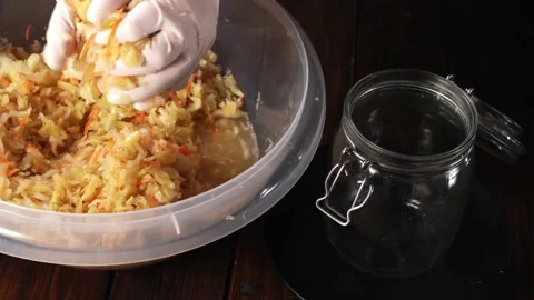 Fermented cabbage. Hands in gloves placing ready sauerkraut in a glass jar Stock Footage 145160252
