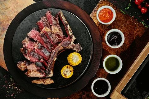 Fermented steak. T-Bone Steak with grilled vegetables on a black round plate on Stock Photos