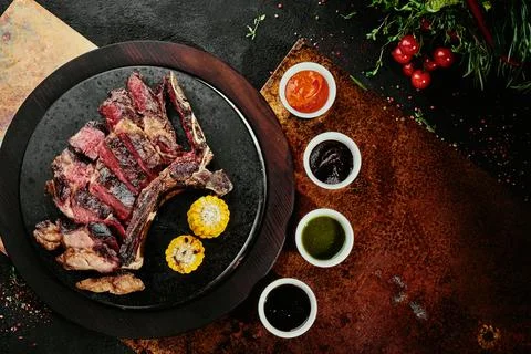 Fermented steak. T-Bone Steak with grilled vegetables on a black round plate on Stock Photos