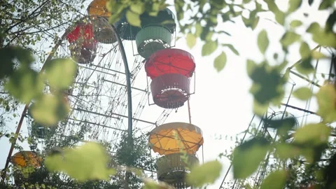 Ferris wheel cabins seen through green leaves in summer amusement park Stockbeeldmateriaal 319535091