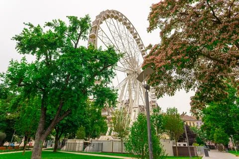 Ferris wheel featuring colourful seating pods against backdrop sky and green Stock Photos