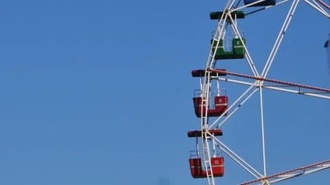 A ferris wheel in motion with empty colorful cabins turning against blue sky Stock Footage 318684162