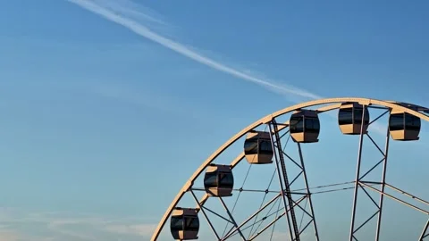 Ferris wheel spinning cabins against a clear blue sky at an amusement park Stock Footage 337791209