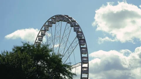 A Ferris wheel spins against a backdrop of trees and a blue sky. City Stock Footage 322170079