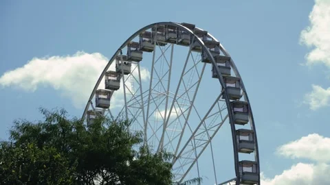 A Ferris wheel spins against a backdrop of trees and a blue sky. City Stock Footage 326484416