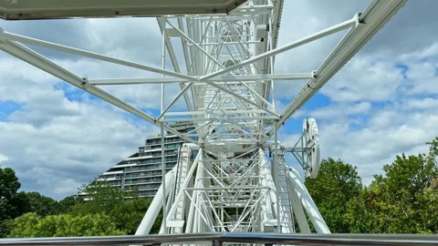 Ferris wheel structure under a cloudy sky with greenery in the background Stock Footage 344787545