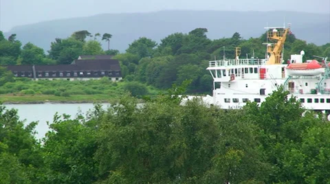 Ferry advancing to the left on a loch or fjord, seen behind tree crowns Stock Footage 39815856