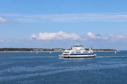 Ferry navigating through calm waters with distant shoreline and sailboats under Stock Photos