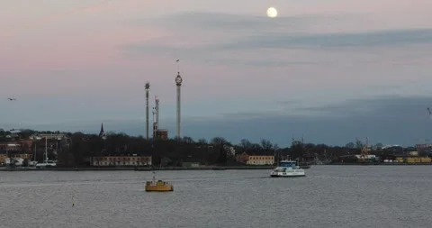 Ferry passes Gröna Lund under a pastel dusk sky with rising full moon Stock Footage 320169493