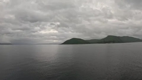 Ferry POV view sailing past lush green coastal hills under cloudy overcast sky Stock-Footage 341814654