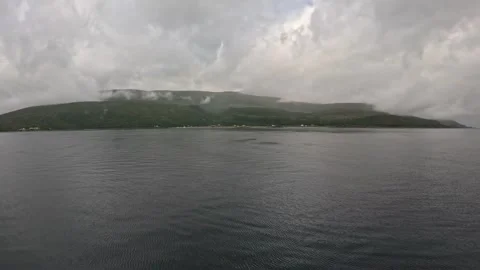Ferry POV view of small coastal village under green cloudy mountain in Norway Stock-Footage 341814643