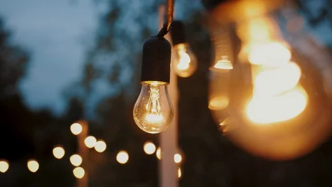 Festival decorative string lights hang and glow outdoors at night Stock Footage