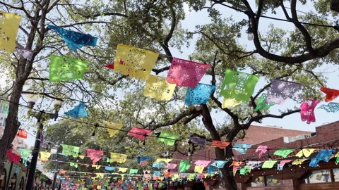 Festive banners hang from trees, swaying gently at Market Square in San Ant.. 動画素材 344906853