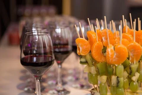 Festive buffet at the event with desert, red wine and skewers of kiwi and man Stock Photos