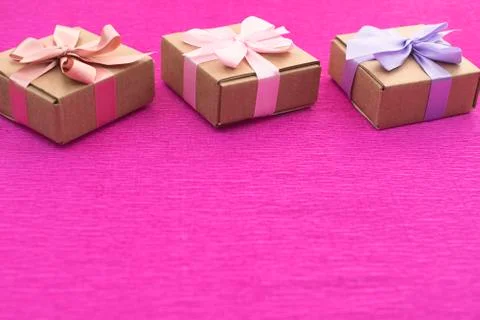Festive composition three Kraft boxes with gifts on bright pink background. Stock Photos