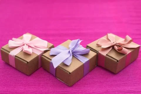 Festive composition three Kraft boxes with gifts on bright pink background. Stock Photos