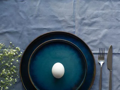 Festive Easter table setting with egg and flowers on blue background Stock Photos