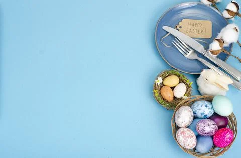 Festive Easter table setting with painted eggs on blue background. Space for  Stock Photos